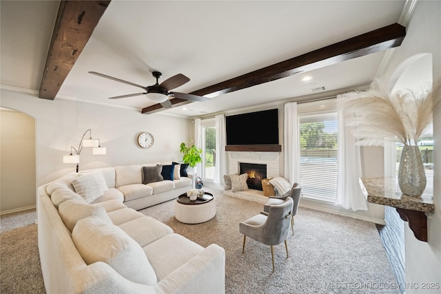 14400 E Willow Way, Claremore, OK 74019 - living room with light colored carpet, beam ceiling, a warm lit fireplace, arched walkways, and ceiling fan