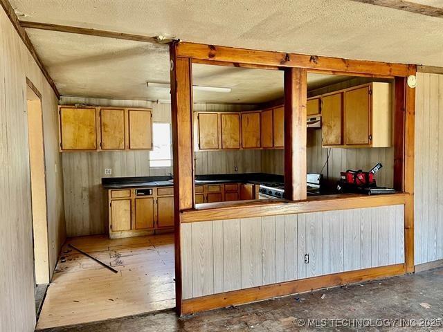 100 W Walnut Ave, Coalgate, OK 74538 - kitchen with range with gas cooktop, brown cabinetry, wood walls, a textured ceiling, and dark countertops