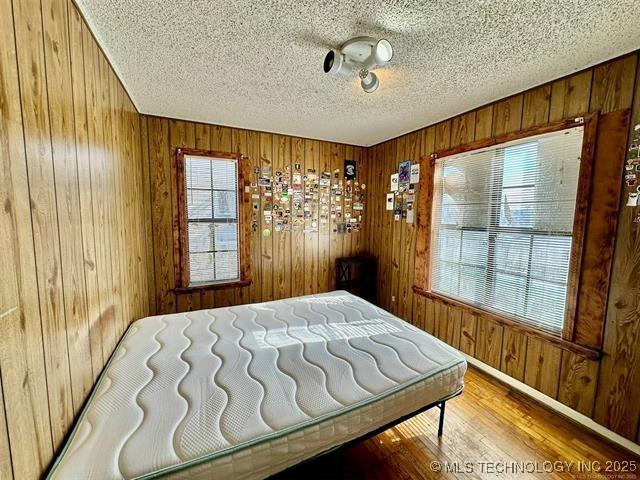 1305 7th Ave NW, Ardmore, OK 73401 - bedroom featuring wooden walls, a textured ceiling, and wood finished floors