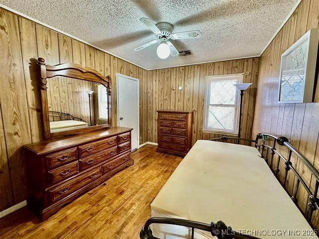 1305 7th Ave NW, Ardmore, OK 73401 - bedroom featuring wood finished floors, wooden walls, a textured ceiling, and a ceiling fan