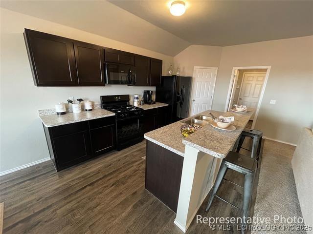 27310 E 117th Pl S, Coweta, OK 74429 - kitchen with black appliances, lofted ceiling, dark wood-style floors, an island with sink, and a kitchen bar