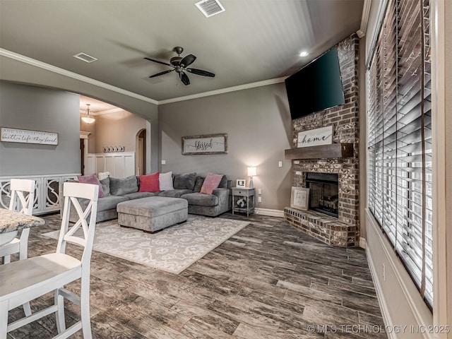 7616 E 84th St, Owasso, OK 74021 - living area with arched walkways, a ceiling fan, a brick fireplace, dark wood-style flooring, and crown molding