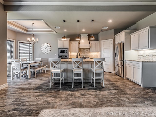 7616 E 84th St, Owasso, OK 74021 - kitchen featuring appliances with stainless steel finishes, premium range hood, a chandelier, backsplash, and dark wood-type flooring