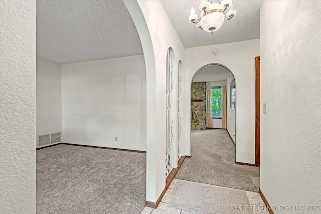 1020 Lariat Dr, Bartlesville, OK 74006 - hallway with arched walkways, carpet flooring, a chandelier, a textured ceiling, and a textured wall