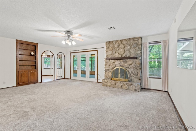 1020 Lariat Dr, Bartlesville, OK 74006 - unfurnished living room featuring a textured ceiling, carpet flooring, ceiling fan, and a stone fireplace