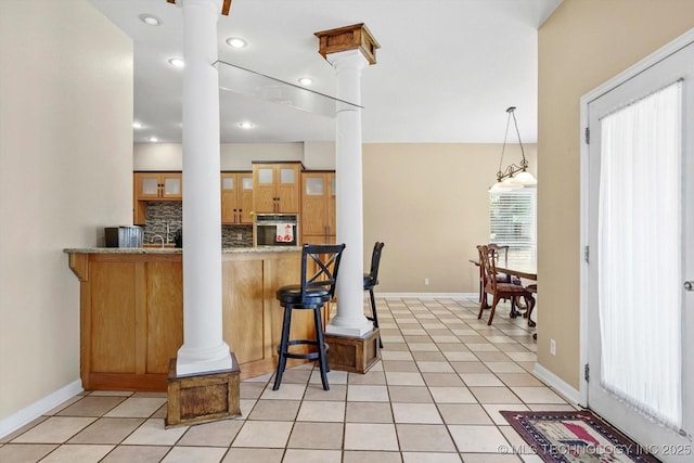 524 S 67th St, Broken Arrow, OK 74014 - kitchen with decorative columns, stainless steel oven, decorative backsplash, a kitchen bar, and light tile patterned floors
