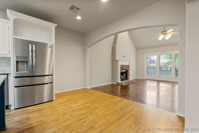 9929 S 85th E Ave, Tulsa, OK 74133 - unfurnished living room featuring a ceiling fan, vaulted ceiling, light wood-type flooring, a brick fireplace, and arched walkways