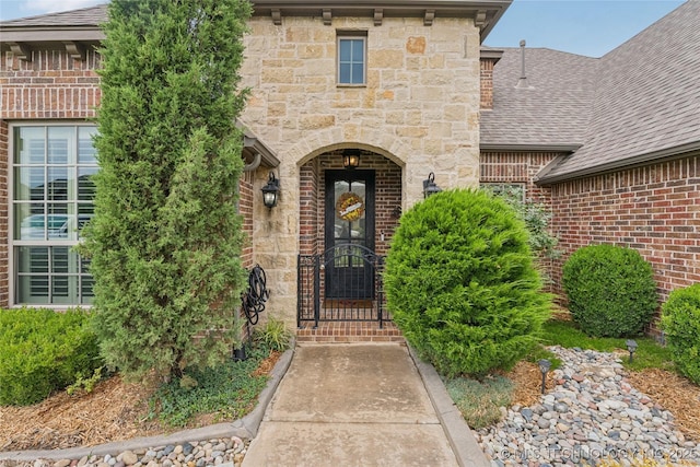 7722 N 142nd Ave E, Owasso, OK 74055 - doorway to property featuring a shingled roof, brick siding, and stone siding