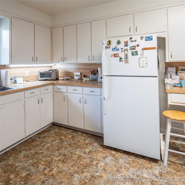1508 E Seminole Ave, Mcalester, OK 74501 - kitchen featuring freestanding refrigerator, stone finish floors, backsplash, and white cabinets