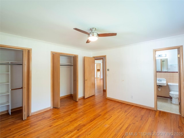 1508 E Seminole Ave, Mcalester, OK 74501 - unfurnished bedroom featuring two closets, light wood finished floors, ensuite bath, ornamental molding, and ceiling fan
