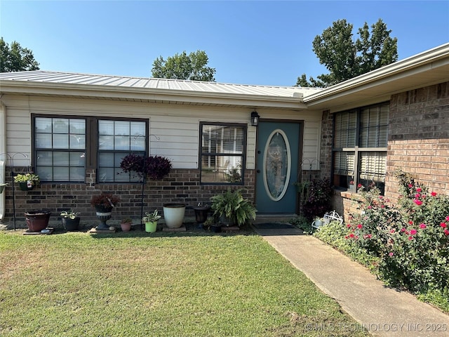 1203 NW 5th St, Stigler, OK 74462 - view of exterior entry featuring a yard, brick siding, a metal roof, and a standing seam roof
