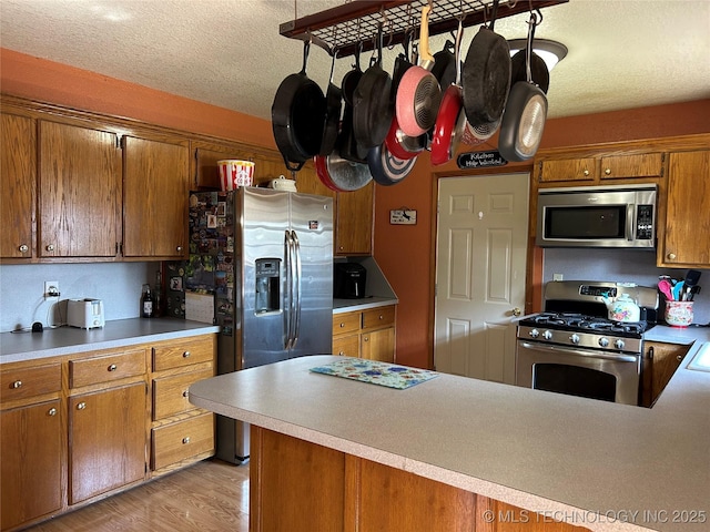 1203 NW 5th St, Stigler, OK 74462 - kitchen featuring appliances with stainless steel finishes, brown cabinets, a textured ceiling, light countertops, and light wood finished floors