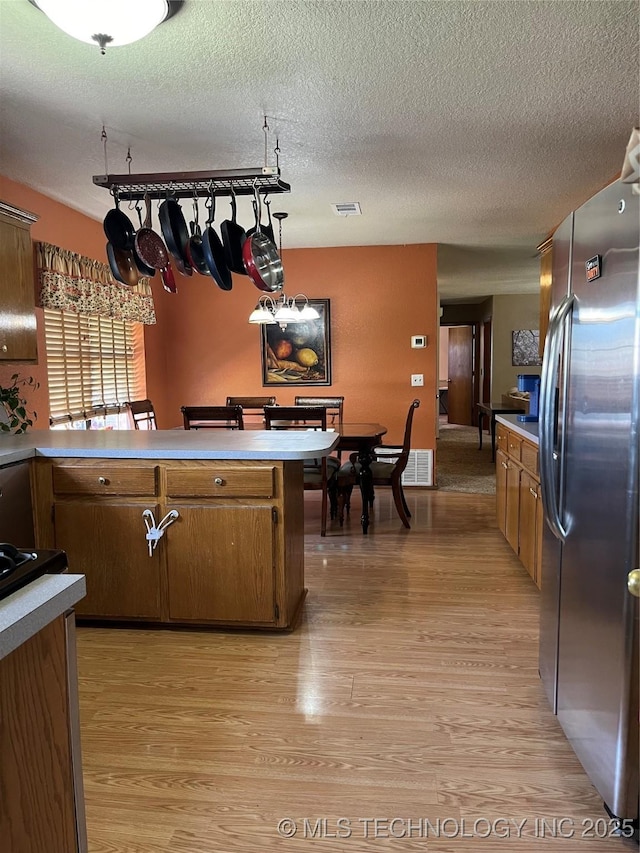 1203 NW 5th St, Stigler, OK 74462 - kitchen with freestanding refrigerator, light wood finished floors, light countertops, a peninsula, and brown cabinets