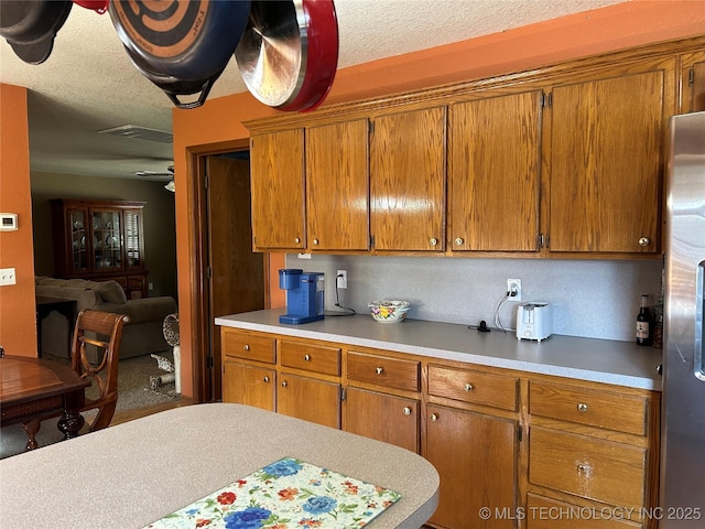 1203 NW 5th St, Stigler, OK 74462 - kitchen featuring stainless steel refrigerator, light countertops, brown cabinetry, and a textured ceiling
