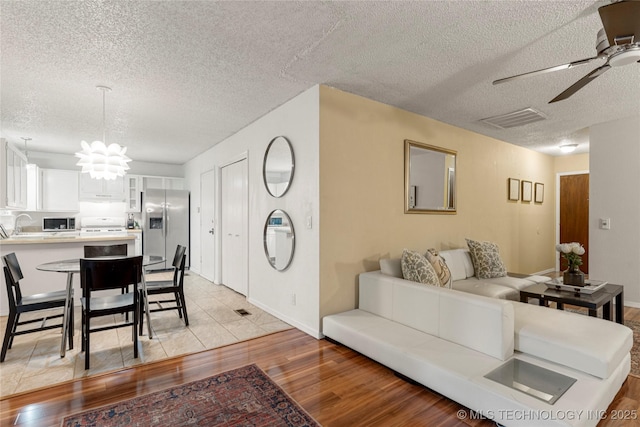 4504 S Cedar Ave, Broken Arrow, OK 74011 - living area featuring a textured ceiling, ceiling fan, light wood-style flooring, and a chandelier