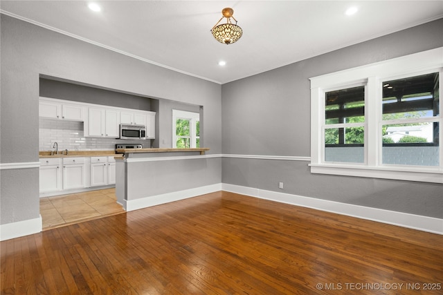 575 N 7th St, Muskogee, OK 74401 - kitchen with stainless steel microwave, white cabinetry, tasteful backsplash, light wood-type flooring, and crown molding