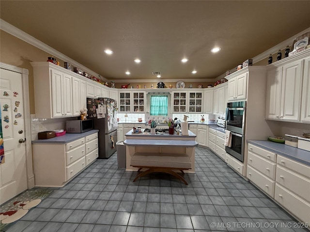 607 Nelson, Mcalester, OK 74501 - kitchen featuring appliances with stainless steel finishes, crown molding, a center island, white cabinetry, and glass insert cabinets