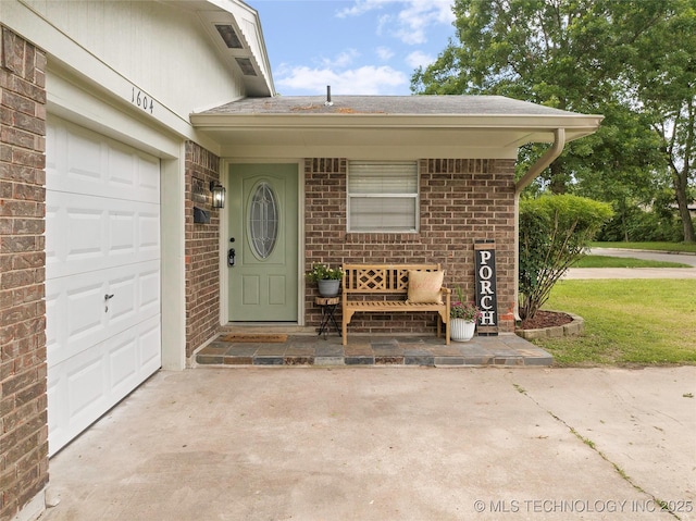 1604 9th Ave NW, Ardmore, OK 73401 - view of exterior entry with driveway, brick siding, a garage, and roof with shingles