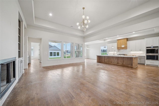 2614 E 134th Cir S, Bixby, OK 74008 - unfurnished living room featuring a chandelier, light wood-style floors, a raised ceiling, recessed lighting, and built in shelves