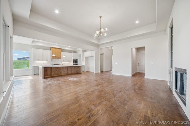 2614 E 134th Cir S, Bixby, OK 74008 - unfurnished living room with a chandelier, a tray ceiling, light wood-type flooring, and recessed lighting