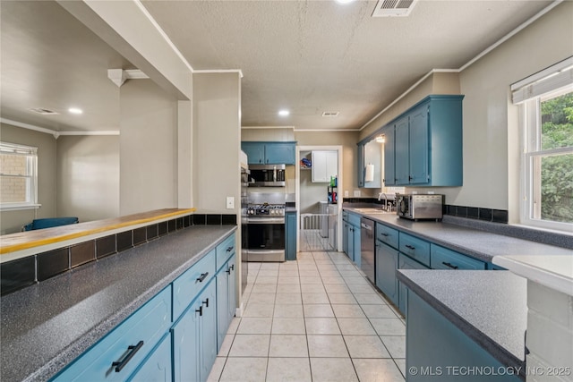 810 N 3rd St, Jenks, OK 74037 - kitchen featuring stainless steel appliances, blue cabinets, dark countertops, light tile patterned floors, and ornamental molding