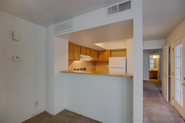 1730 E 67th St Unit K102, Tulsa, OK 74136 - kitchen featuring under cabinet range hood, freestanding refrigerator, light colored carpet, decorative backsplash, and brown cabinetry