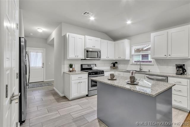 1332 N Denver Ave, Tulsa, OK 74106 - kitchen with stainless steel appliances, white cabinetry, a kitchen island, lofted ceiling, and light stone countertops