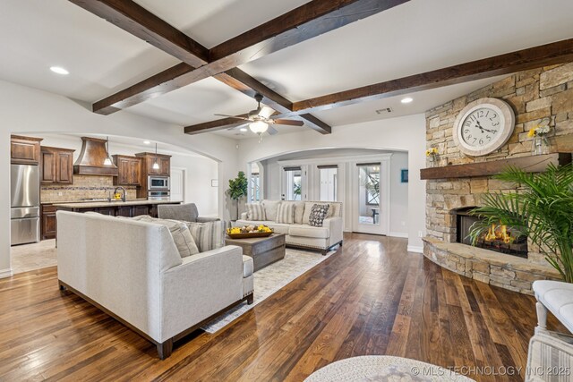 1956 E 172nd St S, Mounds, OK 74047 - living room featuring beamed ceiling, hardwood / wood-style flooring, a ceiling fan, arched walkways, and a stone fireplace