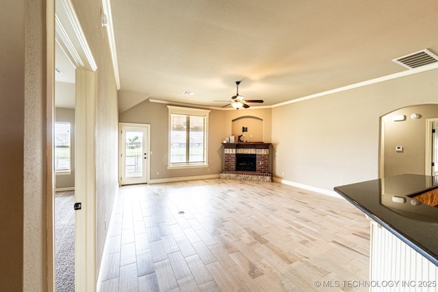 18312 E 46th St, Tulsa, OK 74134 - unfurnished living room featuring arched walkways, ceiling fan, a fireplace, crown molding, and light wood finished floors