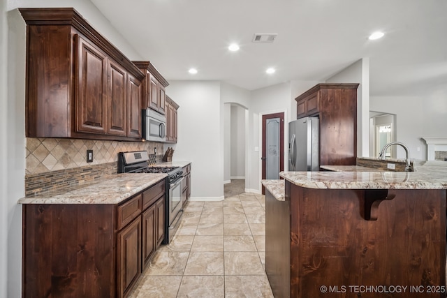 1620 E Boston Ct, Broken Arrow, OK 74012 - kitchen with stainless steel appliances, tasteful backsplash, a breakfast bar area, light stone counters, and arched walkways