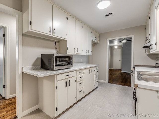 4512 SE Frank Phillips Blvd, Bartlesville, OK 74006 - kitchen with stainless steel microwave, ceiling fan, white cabinets, range with electric stovetop, and light wood-style floors