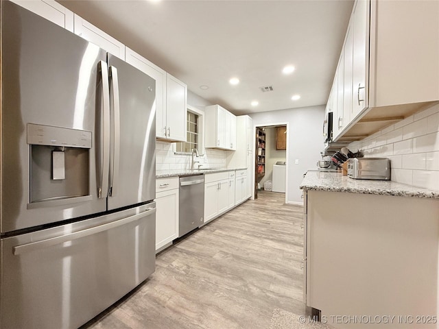 1604 N 2nd Ave, Warner, OK 74469 - kitchen featuring appliances with stainless steel finishes, decorative backsplash, light wood-type flooring, washer / clothes dryer, and white cabinets