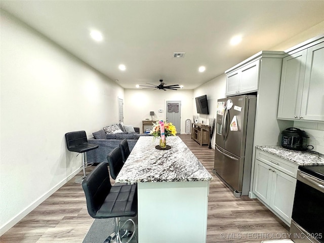 2125 N Lansing Ave W, Tulsa, OK 74106 - kitchen featuring appliances with stainless steel finishes, a ceiling fan, light stone counters, a kitchen island, and a kitchen breakfast bar