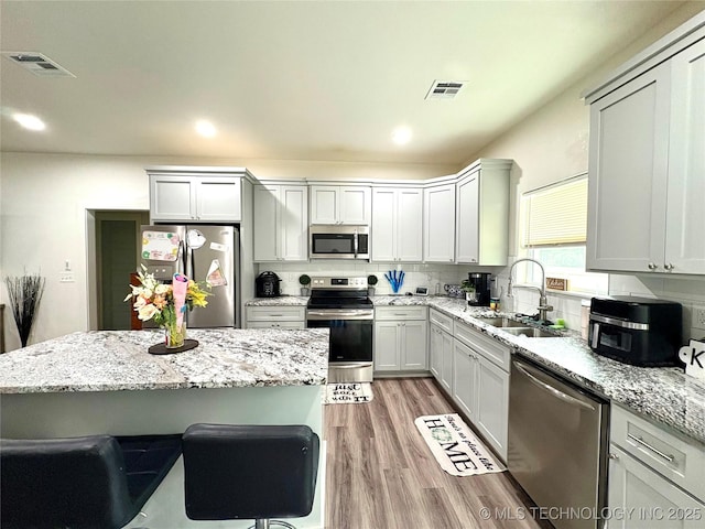2125 N Lansing Ave W, Tulsa, OK 74106 - kitchen with stainless steel appliances, light wood-type flooring, backsplash, a kitchen bar, and light stone counters