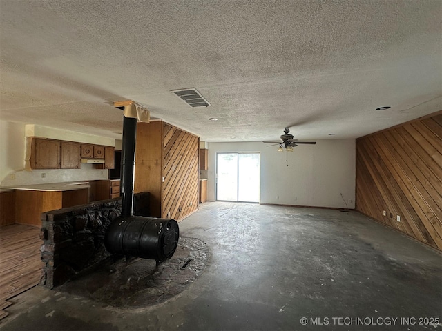 51698 W 139th St S, Drumright, OK 74030 - unfurnished living room featuring wooden walls, a wood stove, concrete flooring, a textured ceiling, and ceiling fan