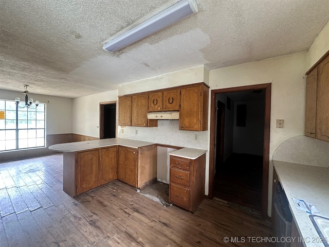 51698 W 139th St S, Drumright, OK 74030 - kitchen featuring a textured ceiling, brown cabinetry, wood finished floors, a chandelier, and a wainscoted wall