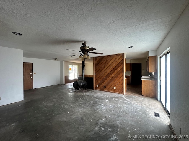 51698 W 139th St S, Drumright, OK 74030 - unfurnished living room featuring concrete flooring, a textured ceiling, ceiling fan, and a wood stove