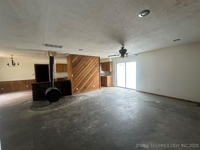 51698 W 139th St S, Drumright, OK 74030 - unfurnished living room with unfinished concrete flooring, wooden walls, a textured ceiling, a wood stove, and ceiling fan