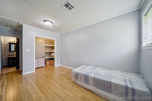 9025 N 156th Rd, Beggs, OK 74421 - bedroom with light wood-type flooring, attic access, crown molding, a textured ceiling, and a walk in closet