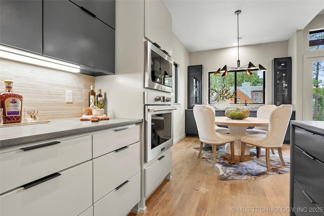 3008 S Boston Ct, Tulsa, OK 74114 - kitchen featuring appliances with stainless steel finishes, backsplash, light wood-type flooring, white cabinetry, and pendant lighting