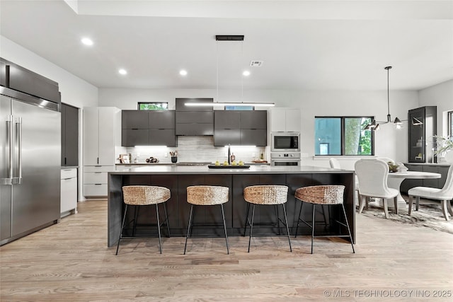 3008 S Boston Ct, Tulsa, OK 74114 - kitchen with built in appliances, modern cabinets, wall chimney exhaust hood, decorative backsplash, and light wood-type flooring