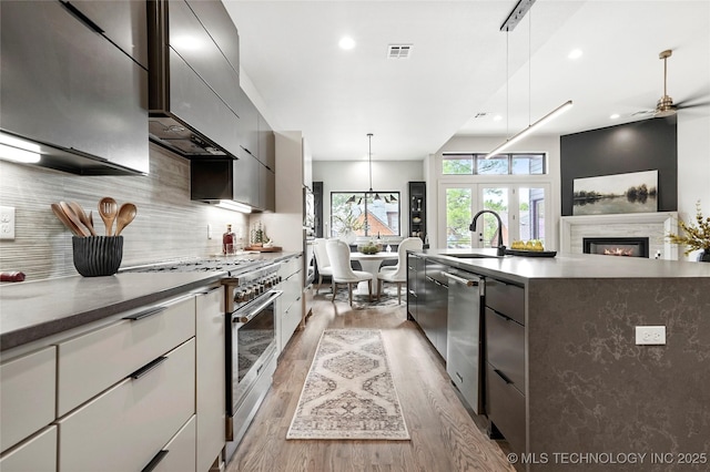 3008 S Boston Ct, Tulsa, OK 74114 - kitchen with appliances with stainless steel finishes, light wood-style floors, backsplash, a center island with sink, and a glass covered fireplace