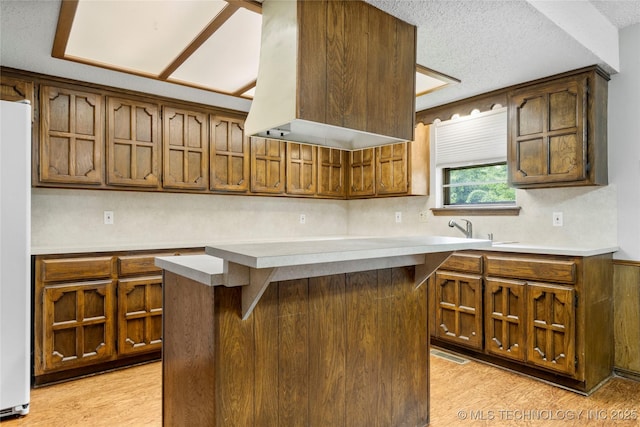 911 N Fir St, Jenks, OK 74037 - kitchen with light countertops, a textured ceiling, light wood-type flooring, a center island, and brown cabinets