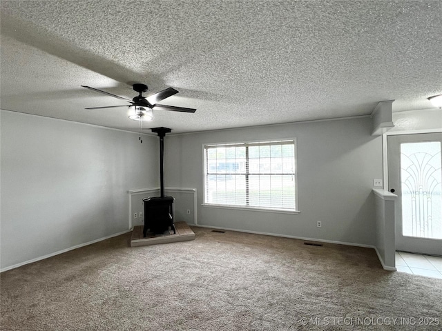 619 W 4th St, Skiatook, OK 74070 - unfurnished living room featuring carpet flooring, a wood stove, ceiling fan, and a textured ceiling