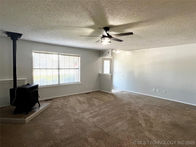 619 W 4th St, Skiatook, OK 74070 - unfurnished living room featuring a wood stove, ceiling fan, plenty of natural light, carpet floors, and a textured ceiling