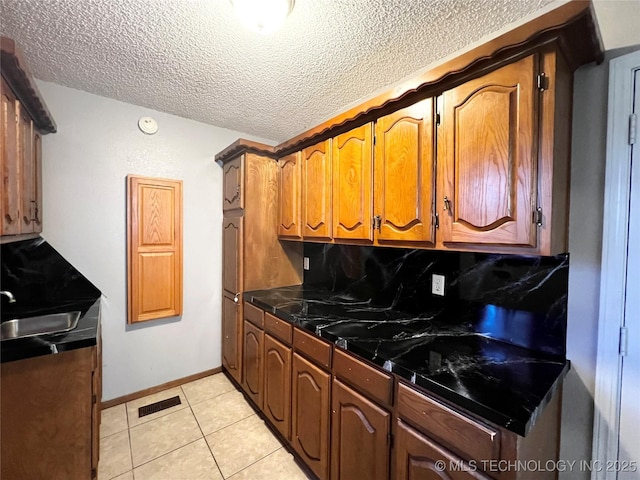 619 W 4th St, Skiatook, OK 74070 - kitchen featuring backsplash, dark countertops, a textured ceiling, light tile patterned floors, and brown cabinets
