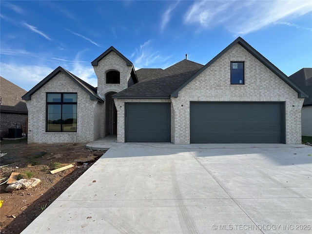 23191 E 107th St, Broken Arrow, OK 74014 - french country home featuring concrete driveway, brick siding, an attached garage, and roof with shingles