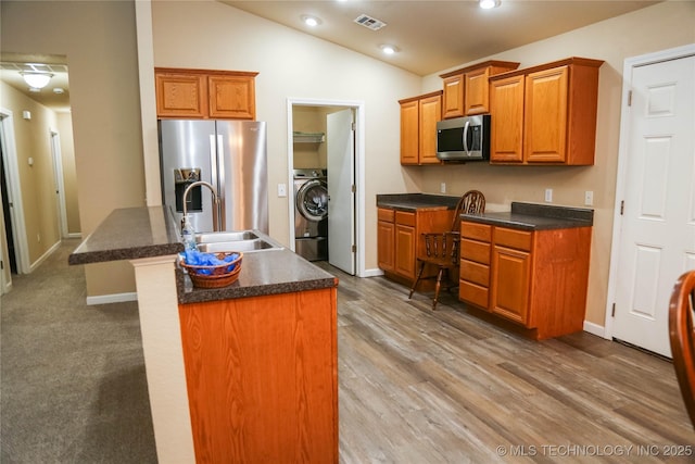 614 S Seminole St, Skiatook, OK 74070 - kitchen featuring stainless steel appliances, washer / dryer, dark countertops, an island with sink, and vaulted ceiling