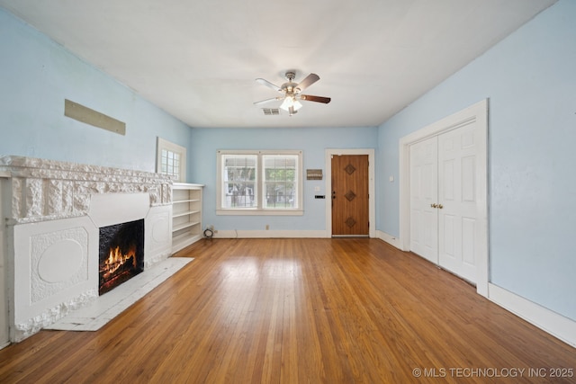 1414 E 8th St, Okmulgee, OK 74447 - unfurnished living room featuring a warm lit fireplace, hardwood / wood-style floors, and ceiling fan