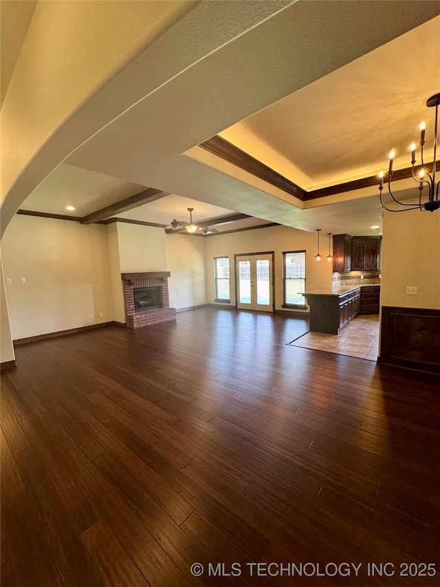 5510 Cooper Ct, Bartlesville, OK 74006 - unfurnished living room with a chandelier, dark wood-type flooring, a brick fireplace, a raised ceiling, and arched walkways